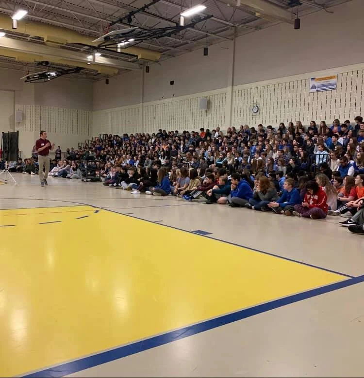 A large student audience gathered for a presentation in a gym