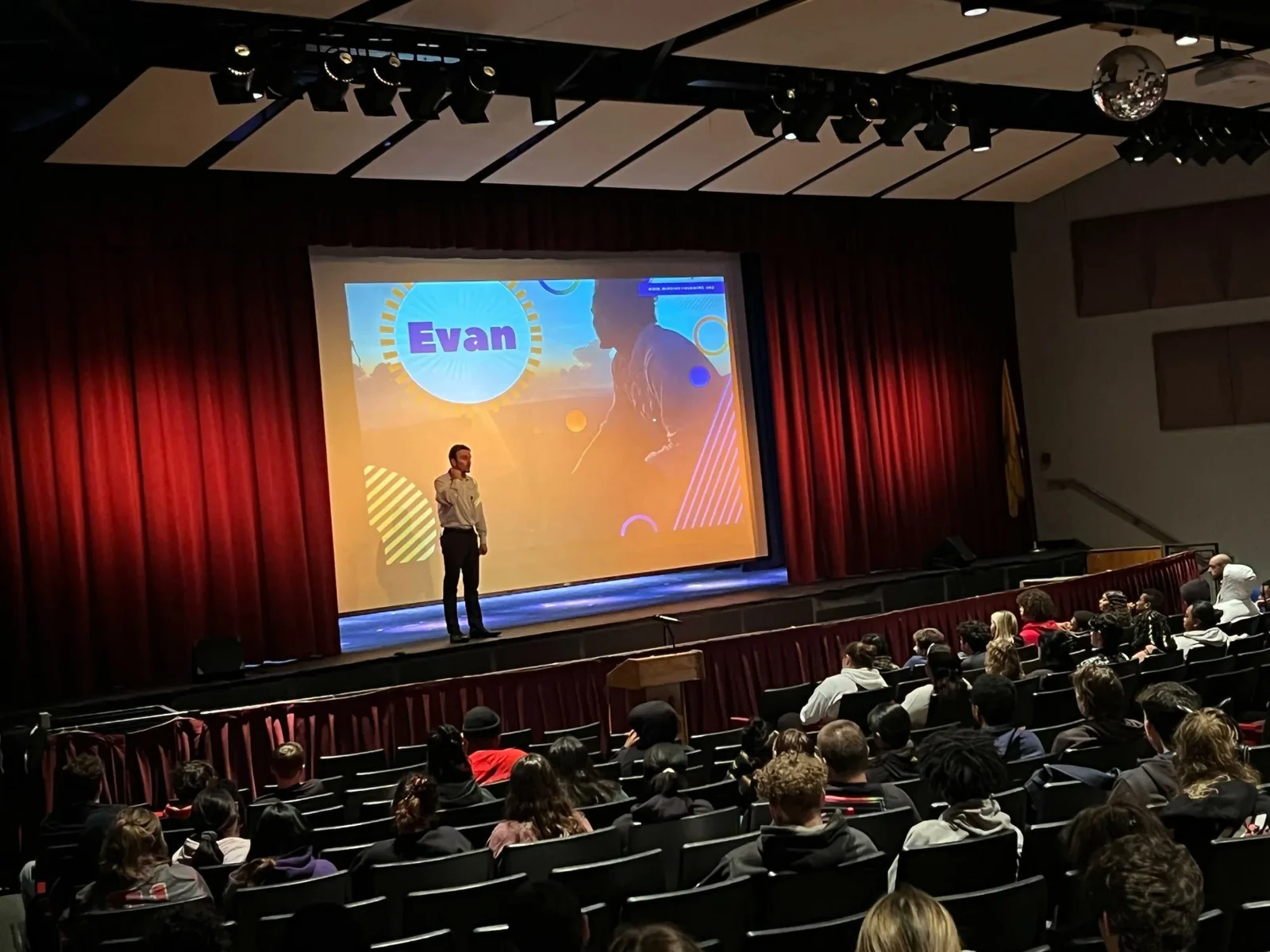 Evan speaking on stage to an auditorium audience